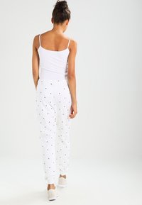 Vita sweatpants med små svarta triangelmönster och elastiska mudd, matchade med en vit linne, bärs med ljusa sneakers.