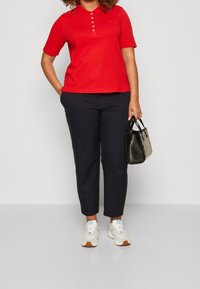 Röd polotröja med korta ärmar och knappslå, kombinerad med marinblå byxor och vita sneakers. Tillbehören inkluderar en svart handväska.