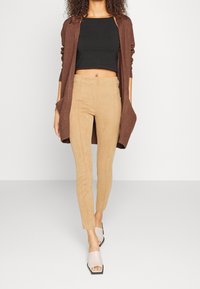 Cardigan largo marrón, top negro corto y pantalones ajustados de ante de tono beige claro. Sandalias de tacón bloque de color beige claro con los dedos al aire. Diseño simple y moderno.