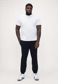 Hvid kortærmet t-shirt i afslappet pasform, kombineret med sorte tætsiddende bukser. Udstyret med hvid og grå sneakers med blå logo-detaljer.