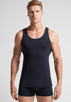 Marineblaues ärmelloses Tanktop aus glattem Stoff; mit rundem Ausschnitt und taillierter Passform, kombiniert mit dunklen Shorts.