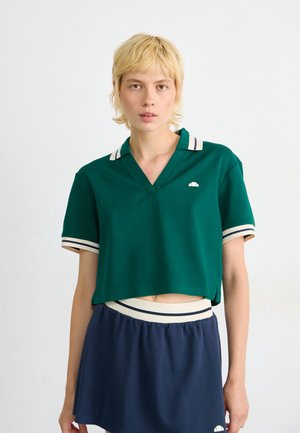 Polo vert raccourci avec un col en V, orné de rayures crème sur le col et les manches, associé à une jupe marine.