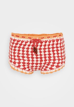 Punane ja valge heegeldatud lühikesed püksid, millel on laineline äär, oranž joonkinnitus ja ees puidust detailid.