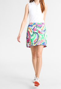 Sukně s vícero barvami a vzory, se spirálami růžové, zelené a modré; lehká tkanina, délka nad kolena; spárována s bílým bezrukávovým polo.