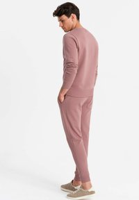 Helles Mauve Sweatshirt mit gerippten Bündchen und Saum, kombiniert mit passenden Jogginghosen mit seitlichen Taschen. Model trägt hellgraue Sneakers.