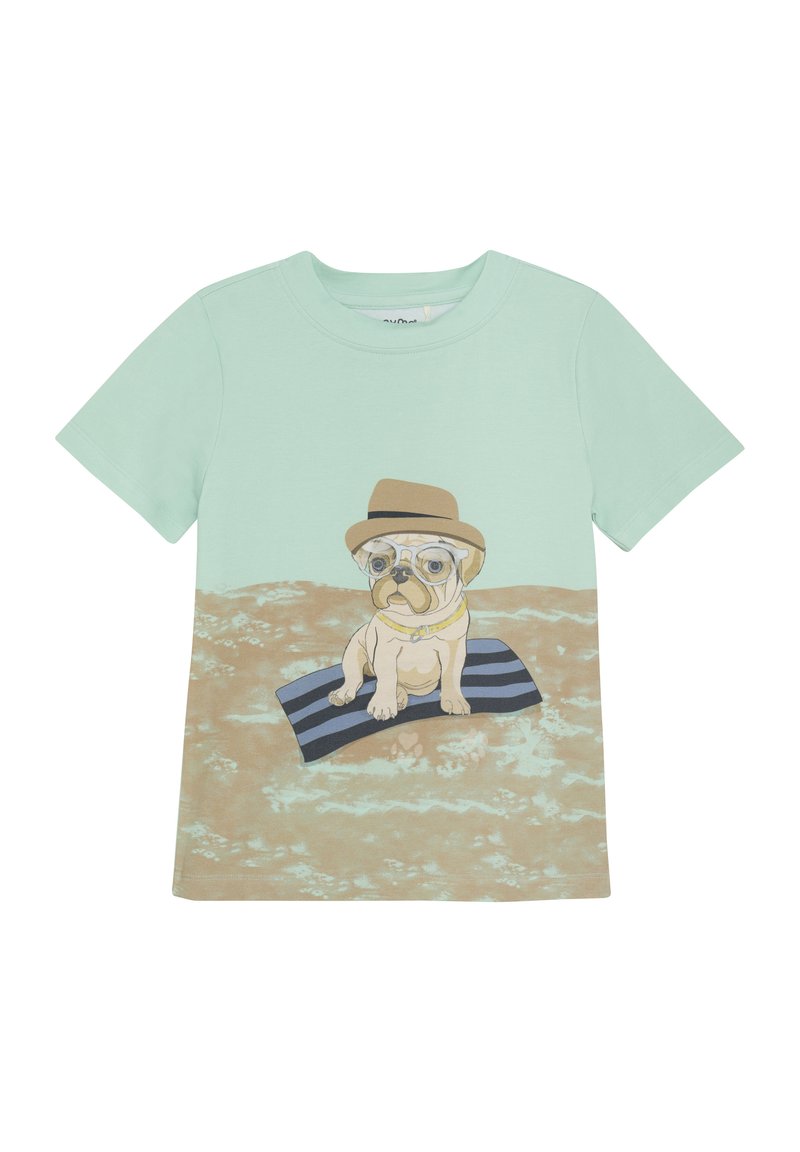 Mintgrön t-shirt med en grafik av en mops som sitter på en randig matta, iklädd glasögon och hatt, mot en sandig bakgrund.