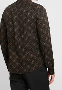 Camicia nera a maniche lunghe con motivo floreale in tonalità terrestri, dotata di colletto a polo e polsini con bottoni. Tessuto liscio, vestibilità su misura.