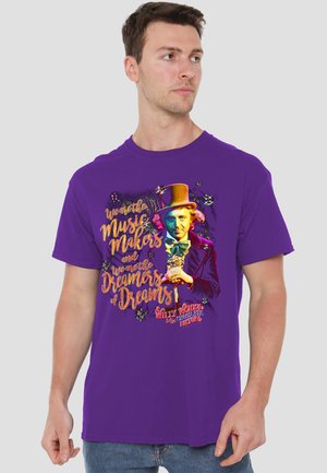 Man wearing a purple T-shirt with colorful Willy Wonka illustration and text "We are the Music Makers and we are the Dreamers of Dreams."