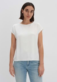 Top bianco a maniche corte con scollatura rotonda, dalla texture liscia, con una vestibilità comoda, abbinato a jeans azzurri chiari. Design minimalista, senza motivi.