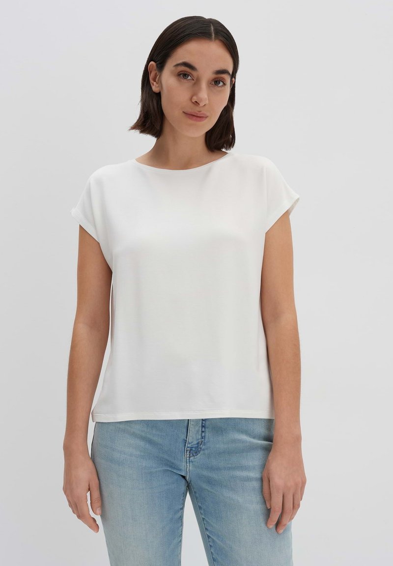 Top bianco a maniche corte con scollatura rotonda, dalla texture liscia, con una vestibilità comoda, abbinato a jeans azzurri chiari. Design minimalista, senza motivi.