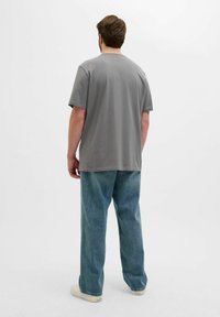 Camiseta de algodón gris con un corte relajado, mangas cortas y cuello redondo, combinada con pantalones de mezclilla azul claro y zapatillas blancas.