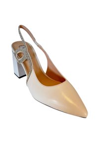 Pump beige con strap allacciata e punta affilata, caratterizzata da una fascia decorata con cristalli e un tacco quadrato. Texture in pelle liscia, design elegante.