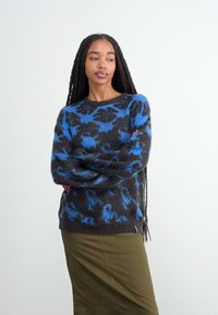 Maglione a pattern blu e nero con scollo a girocollo, polsini a coste e finitura testurizzata, abbinato a una gonna verde.