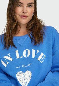 Sudadera azul con el texto "ENAMORADO" en blanco, con un gráfico de un corazón debajo. El material parece suave, con un corte relajado y diseño de cuello redondo.