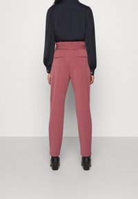 Hoge taille, roze broek met een gerimpelde riem, twee achterzakken en taps toelopende pijpen. Draag het met een marineblauwe blouse en zwarte hakken.