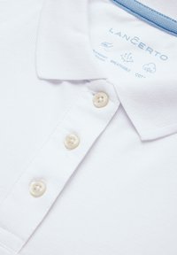 Biała koszulka polo z teksturowanej tkaniny, z niebieskim akcentem na kołnierzyku. Zawiera cztery kremowe guziki oraz metkę z instrukcjami pielęgnacji.