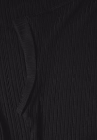 Zbliżenie na czarną, żebrowaną tkaninę z zagiętym brzegiem, ukazującą pionowe teksturowane linie oraz miękkie detale dzianiny.