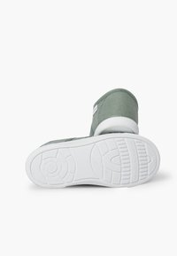 Sneaker verde in tela con superficie texture, suola in gomma bianca e un piccolo tag con logo. Caratterizzato da punta rotonda e design low-top.