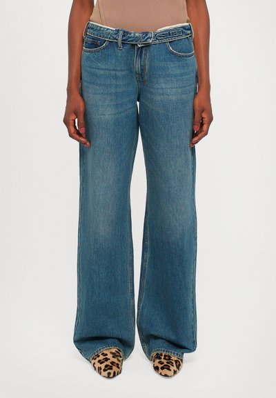 Jean en denim bleu à taille haute et jambes larges, avec passants de ceinture et un lavage délavé, associés à des chaussures à bout pointu en imprimé léopard.