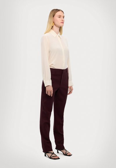 Bluză din krem ușor, cu buton, purtată cu pantaloni burgundici ajustați, completată de sandale negre cu bretele. Material neted, design clasic al gulerului.