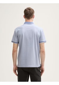 Ljusblå polo med klassisk krage, korta ärmar med matchande kant och ett slätt, texturerat tyg. Enkel design, inga mönster.