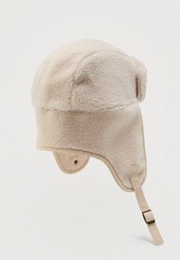 Chapeau en fausse fourrure de mouton, de couleur beige clair. Doté de rabats pour les oreilles, d'une couronne ronde et d'une sangle avec une boucle pour un maintien sécurisé. Texture douce.