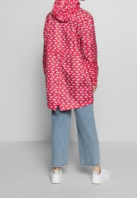 Czerwona wodoodporna kurtka z powtarzającym się białym wzorem psów, z długimi rękawami, kapturem i prostym krojem, zestawiona z jasnoniebieskimi spodniami o szerokich nogawkach.