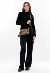 Top a maniche lunghe nera abbinato a pantaloni neri a gamba larga. Gli accessori includono una piccola borsa a tracolla con stampa leopardata e un ciondolo a forma di zip rotondo.