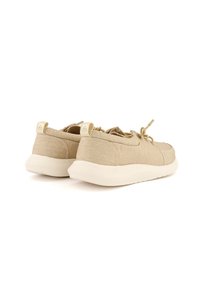 Beige Stoff-Sneaker mit einem weichen, strukturierten Obermaterial, elastischen Schnürsenkeln und einer weißen, gepolsterten Sohle. Auf der Rückseite befindet sich ein kleines Markentag.