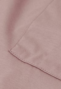 Světle růžová látka s hladkým povrchem, s plochým švem a čtvercovým detailem. Detailní záběr zdůrazňuje měkkost materiálu.