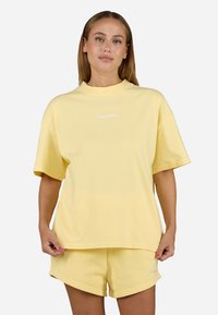 Gul bomull T-skjorte med avslappet passform, kort erm, og lite hvitt logo, kombinert med matchende gule shorts. Glatt tekstur.