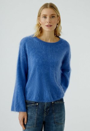 Blaues Mohair-Mischpullover mit Rundhalsausschnitt und langen, weit ausgestellten Ärmeln; weiche, flauschige Textur; kombiniert mit hoch taillierten Jeans.