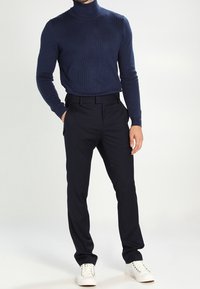 Marinblå ribbad polotröja med figurnära passform, kombinerad med skräddarsydda svarta byxor och vita sneakers, vilket skapar en modern och strömlinjeformad look.