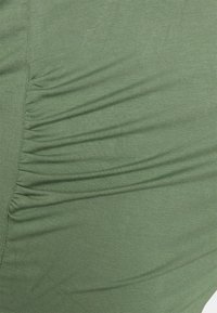 Tecido verde com uma textura suave, apresentando detalhes franzidos de um lado, criando pregas subtis e uma silhueta ajustada.