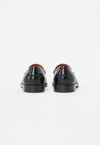 Zwarte lederen schoenen hebben een glanzend krokodillenpatroon, een ronde neus en dunne, vlakke zolen. De binnenkant heeft een contrasterende rode kleur.