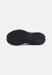 Semelle de chaussure de sport noire avec un motif de crampons robuste pour une meilleure traction, fabriquée en caoutchouc durable, dotée de diverses rainures et arêtes texturées.
