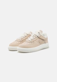 Beige lädersneakers med vita snören och strukturerade detaljer. Har ett perforerat mönster på tån och en vit gummisula med grepp.