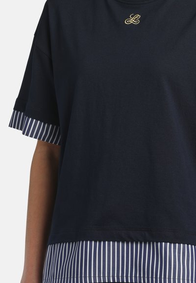 Navy blue short-sleeve top layered over a striped blue and white shirt with a small embroidered gold logo near the neckline.
