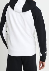 Huvtröja med raglanärmar, prydd med svarta och vita paneler, mjuk textur och logotypdetalj på vänster ärm.
