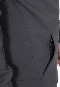 Felpa grigia con tasca e zip nera. Il materiale sembra morbido, con una texture liscia e un design aderente.