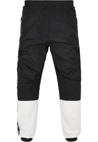 Svart och vit trackpants med elastiskt midjeband, åtdragna ärmslut och sidopaneldetaljer, tillverkade av lätt och mjukt tyg.
