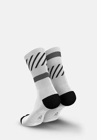 Weiße Socken mit schwarzen Akzenten, die diagonale Streifen und eine durchgehend schwarze Spitze aufweisen. Hergestellt aus einem Stoff mit glatter Textur.