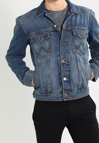 Spijkerjack in donkerblauw met een klassieke snit, voorzien van twee borstzakken, knoopsluitingen en contrasterende stikseldetails.