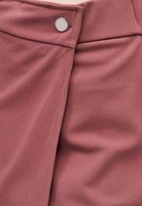 Κοντινό πλάνο υφάσματος σε χρώμα σκόνης τριαντάφυλλου με ασημένιο κουμπί, που δείχνει επικαλυπτόμενα στρώματα και λεπτομέρειες ραφής.