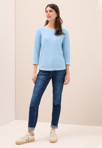 Maglione azzurro chiaro a maniche lunghe abbinato a jeans blu scuro e sneakers beige con dettagli blu. Il maglione ha un collo rotondo e una vestibilità comoda.