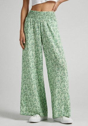Pantalones de pierna ancha color verde claro con estampado floral, cintura fruncida y tela suave. Combinados con zapatillas blancas.