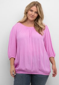 Lys rosa, tekstureret bluse med en bred halsudskæring og puffede ærmer. Elastiske manchetter og nederkant giver en afslappet pasform.