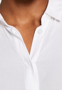 Collet et haut de la poitrine d'une personne portant une chemise blanche à boutons, les deux premiers boutons étant défaits.