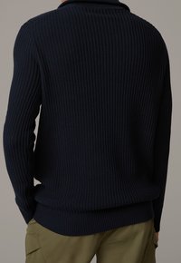 Pull bleu marine côtelé avec col à demi-boutons et tricot texturé ; poignets et ourlet ajustés ; porté avec un pantalon cargo olive.