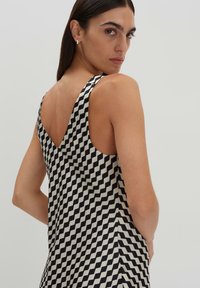 Schwarzes und cremefarbenes ärmelloses Kleid mit Zickzackmuster und tiefem V-Ausschnitt, das eine glatte Textur und eine lockere Passform aufweist.